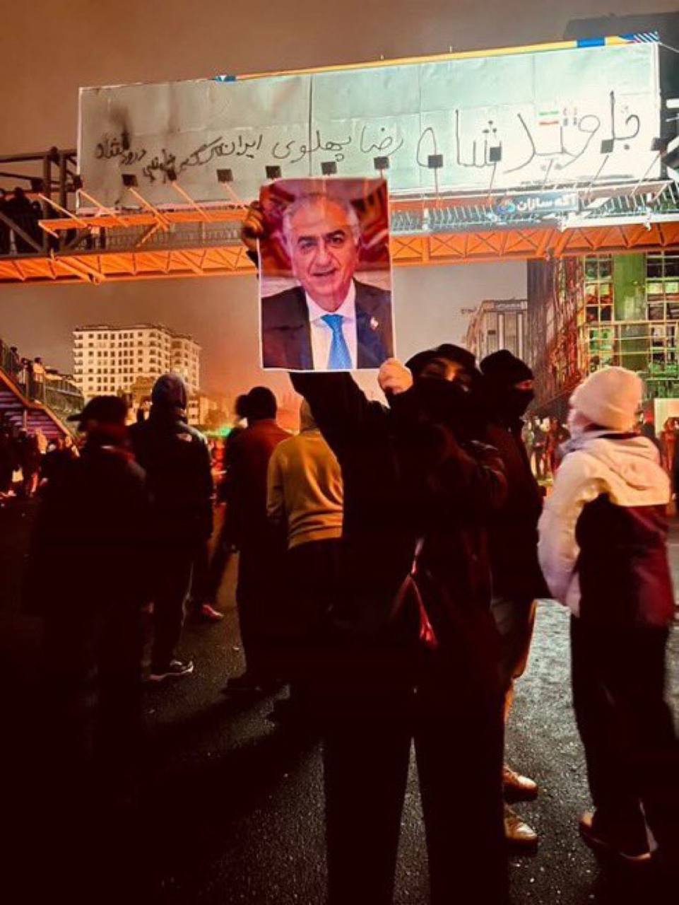 Demonstrator holding a portrait of Reza Pahlavi beneath Persian graffiti