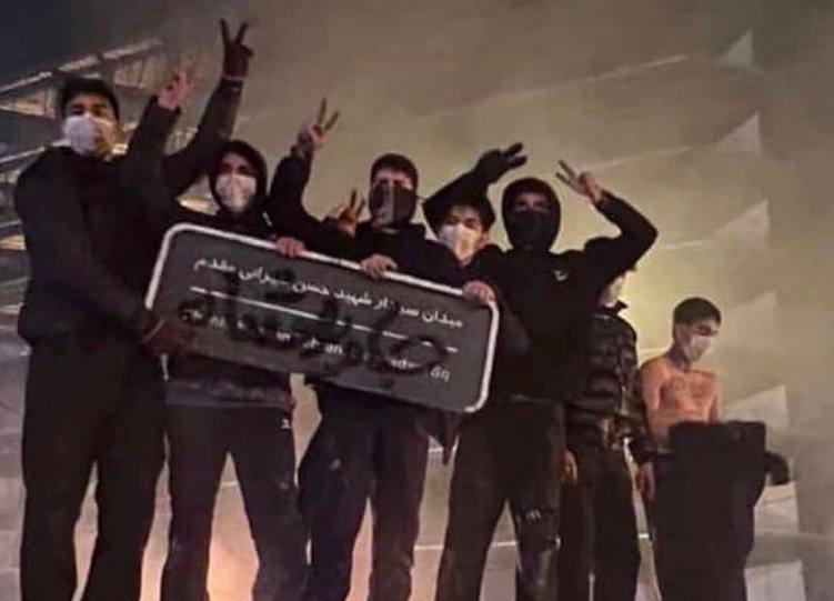Masked protesters holding a Persian street sign and making victory signs